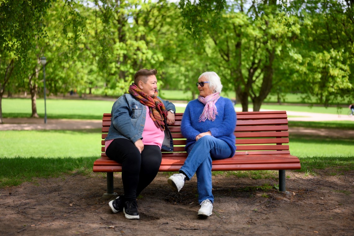 To kvinner snakker på en benk i en park